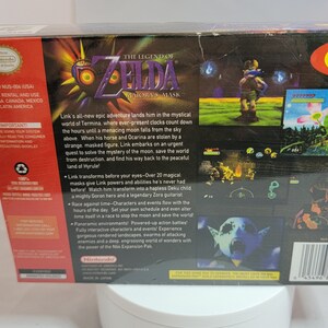 Pu&ograve; includere: Il retro di una scatola di videogiochi per Nintendo 64 per "The Legend of Zelda: Majora's Mask". La scatola &egrave; nera con schermate di gioco colorate e testo che descrive la trama e le caratteristiche del gioco. Il logo Nintendo &egrave; visibile.