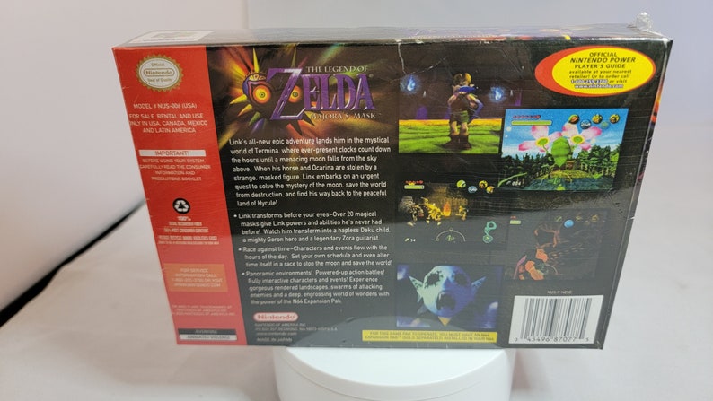 Pu&ograve; includere: Il retro di una scatola di videogiochi per Nintendo 64 per "The Legend of Zelda: Majora's Mask". La scatola &egrave; nera con schermate di gioco colorate e testo che descrive la trama e le caratteristiche del gioco. Il logo Nintendo &egrave; visibile.