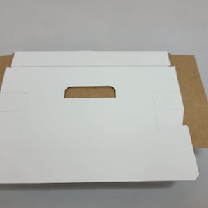 May include: A white cardboard box with a cut-out handle. The box is folded flat and has brown cardboard edges.