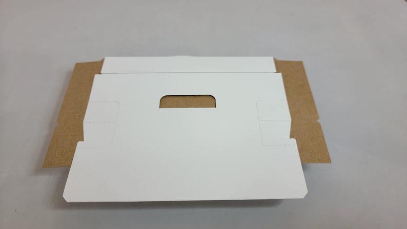 May include: A white cardboard box with a cut-out handle. The box is folded flat and has brown cardboard edges.