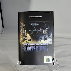 May include: A black and white instruction booklet for the Nintendo 64 video game Star Wars: Shadows of the Empire. The cover features a dark, shadowy image of a character from the game, along with the game's title and the Nintendo 64 logo.