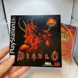 Peut inclure: Bo&icirc;tier de jeu PlayStation pour "Diablo", avec une illustration de d&eacute;mon rouge sur fond noir. Le logo PlayStation et l'&eacute;tiquette "Player's Edition" sont visibles. Le disque de jeu est partiellement visible dans le bo&icirc;tier transparent.