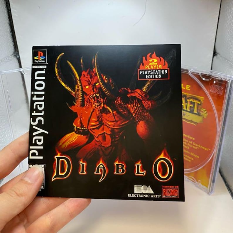 Peut inclure: Bo&icirc;tier de jeu PlayStation pour "Diablo", avec une illustration de d&eacute;mon rouge sur fond noir. Le logo PlayStation et l'&eacute;tiquette "Player's Edition" sont visibles. Le disque de jeu est partiellement visible dans le bo&icirc;tier transparent.
