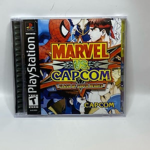 May include: A PlayStation game case for "Marvel vs. Capcom: Clash of Super Heroes." The cover features Spider-Man, Ryu, and other characters. The game case is clear plastic with the PlayStation logo and ESRB rating.