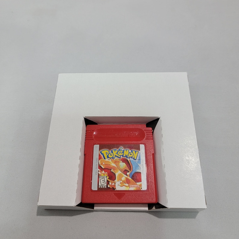 May include: A red Game Boy Color game cartridge with the title "Pok&eacute;mon" printed on the front. The cartridge is in a white cardboard box with a cutout for the cartridge.