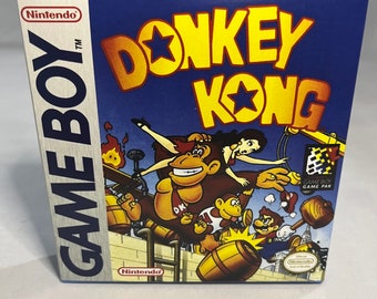 May include: A blue Game Boy game cartridge box with a yellow Donkey Kong title and a colorful illustration of Donkey Kong, Diddy Kong, and a female character. The text "Game Boy Game Pak" is visible on the box.