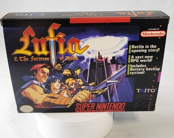 Puede incluir: Una caja de cartucho de juego Super Nintendo para Lufia & The Fortress of Doom. La caja presenta una ilustración colorida de los personajes del juego y una espada. El texto en la caja dice "Lufia & The Fortress of Doom" y "Super Nintendo Entertainment System".