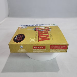 May include: A gold Game Boy Color game cartridge case for The Legend of Zelda: Link's Awakening DX. The case features a gold background with the game's title and logo in white. The case also includes a small image of Link and a sword. The text "Includes New Secret Dungeon!" is printed on the case.