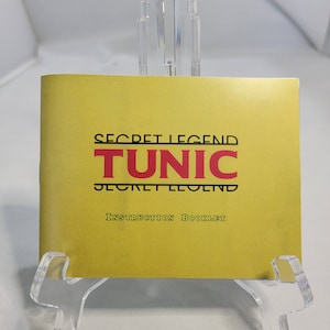 May include: A yellow instruction booklet for the video game "Secret Legend Tunic". The title is in black and red lettering.
