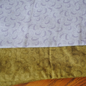 May include: Two pieces of fabric with a repeating pattern of small, stylized leaves. The top fabric is light purple with a white background. The bottom fabric is a dark green with a light brown background.