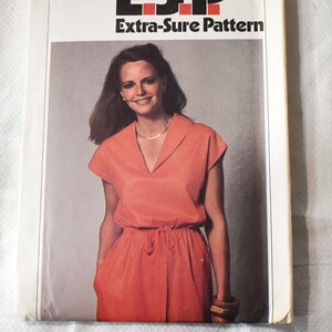 以下が含まれることがあります： ヴィンテージSimplicityのソーイングパターン9022。コーラル色のドレスを着た女性が描かれています。パターンカバーには「ESP Extra-Sure Pattern」の文字と「95¢」の価格が記載されています。ドレスはVネック、半袖、ドローストリングウエストです。