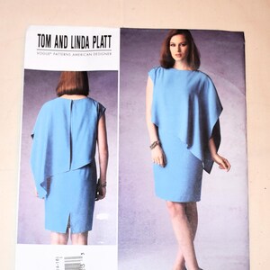May include: A Tom and Linda Platt Vogue Patterns American Designer sewing pattern envelope, model V1373, featuring a light blue sleeveless dress with an asymmetrical draped overlay. The front and back views of the dress are displayed on the packaging.