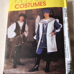 Puede incluir: Un sobre de patrón McCall's Costumes amarillo con ilustraciones de dos trajes medievales. El sobre muestra el número 2802 y texto en inglés y español. Los trajes incluyen túnicas, capas y botas.