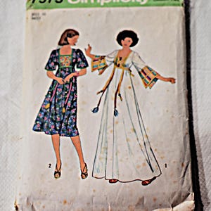 Peut inclure: Une pochette de patron de couture Simplicity 7975 vintage illustrant deux robes. L'une est une robe à fleurs bleu foncé arrivant aux genoux avec des manches courtes, l'autre est une robe blanche longue avec des manches évasées et des bordures colorées.