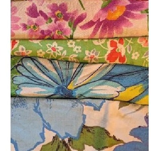 May include: A stack of colorful floral fabric remnants. The fabrics feature various patterns, including red, orange, and yellow flowers, purple and pink blooms, and large blue and green floral designs. The fabrics are folded and stacked.