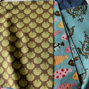 May include: A collection of fabric swatches featuring different patterns. One swatch has a brown background with a repeating pattern of yellow seashells. Another swatch has a blue background with a repeating pattern of brown floral designs. The third swatch has a blue background with a repeating pattern of colorful fish.