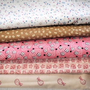 May include: A stack of five fabric swatches featuring different patterns. The top swatch is white with small pink and blue dots. The second swatch is brown with a repeating pattern of small lines. The third swatch is pink with a repeating pattern of small flowers. The fourth swatch is pink and white with a repeating pattern of small squares. The bottom swatch is beige with a repeating pattern of small flowers.