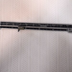 May include: A silver sewing gauge with a sliding marker. The gauge is marked with inches from 1 to 5 and the text "Dritz Sewing Gauge".