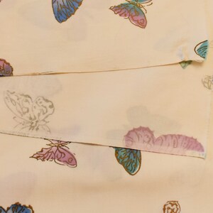 Pu&ograve; includere: Un tessuto color crema con un motivo ripetitivo di farfalle in diverse tonalit&agrave; di blu, rosa e viola.