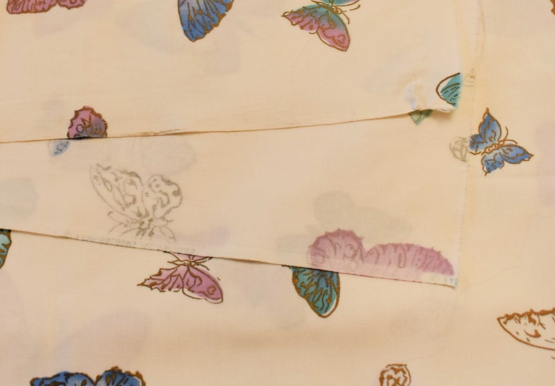 Pu&ograve; includere: Un tessuto color crema con un motivo ripetitivo di farfalle in diverse tonalit&agrave; di blu, rosa e viola.