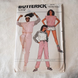 May include: A Butterick 6318 sewing pattern envelope featuring illustrations of activewear, including a pink sweatshirt, sweatpants, and shorts. The text includes Butterick, 6318, Taille/Size 14-16-18, and Jayne Kennedy. The design shows three outfits.