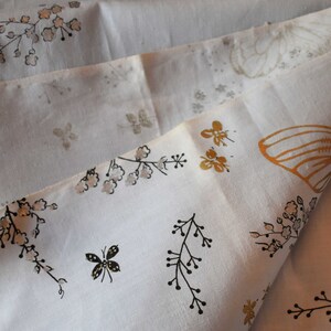 Pu&ograve; includere: Tessuto bianco con un motivo floreale e farfalle. Il tessuto presenta contorni neri di fiori e rami, farfalle dorate e piccoli fiori bianchi.