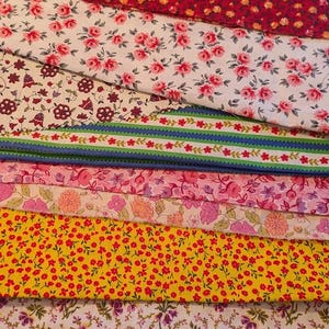 May include: A stack of various fabric swatches with floral patterns. The fabrics feature red, pink, yellow, and purple flowers on white, red, and yellow backgrounds. The text "Hooks, Eyes" is visible on the bottom fabric.