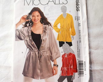 May include: A McCall's sewing pattern envelope, M5635, featuring a woman wearing a silver jacket with a drawstring waist. The envelope also shows illustrations of a yellow hooded top and a red blouse. Size A5 (6-8-10-12-14).