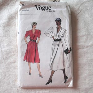 May include: A Vogue Patterns sewing pattern envelope, number 8555, size 14. The white paper envelope features illustrations of two dresses: one in red with short sleeves and one in white with long sleeves, both belted at the waist with a V-neckline.