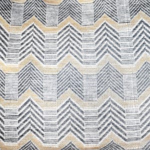 Op de afbeelding: Een close-up van een geweven stof met een chevron-patroon in beige en grijze tinten.