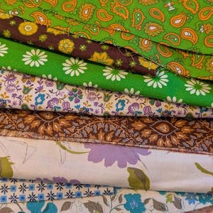 May include: A stack of colorful fabric remnants with various patterns. The fabrics include paisley, floral, and geometric designs in shades of green, brown, purple, blue, and red. These fabrics are suitable for sewing and crafting projects.