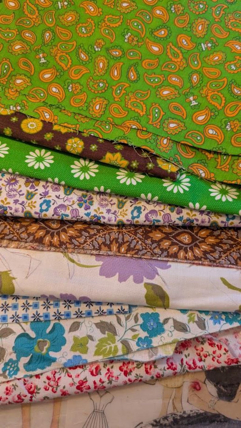 May include: A stack of colorful fabric remnants with various patterns. The fabrics include paisley, floral, and geometric designs in shades of green, brown, purple, blue, and red. These fabrics are suitable for sewing and crafting projects.