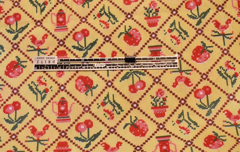 K&ouml;nnte beinhalten: Gelber Stoff mit einem sich wiederholenden Muster aus roten Kirschen, roten Erdbeeren, roten H&auml;hnen, roten Teekannen und roten Topfpflanzen. Der Stoff wird mit einem Lineal gemessen, auf dem "DRITZ Sewing Gauge" steht.