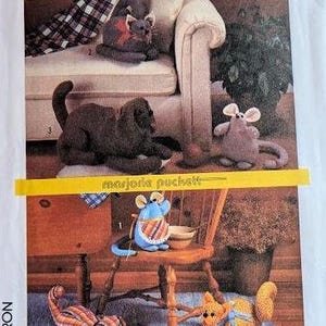 Pode incluir: Um padrão de costura para fazer brinquedos de pelúcia. O padrão inclui instruções para fazer um gato, um cão e um rato. Os brinquedos são mostrados em várias poses em um sofá e uma cadeira.
