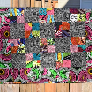 May include: A colorful patchwork quilt with a variety of patterns and colors, including pink, green, blue, and black. The quilt is made up of squares of fabric sewn together.