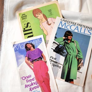 Puede incluir: Una colección de revistas de patrones de costura McCall's vintage. Las portadas presentan ilustraciones de mujeres con ropa elegante. Las revistas son de varios colores, incluyendo verde, morado y rosa, con textos como "April Fashion Digest" y "One's Free Sewing Spree."