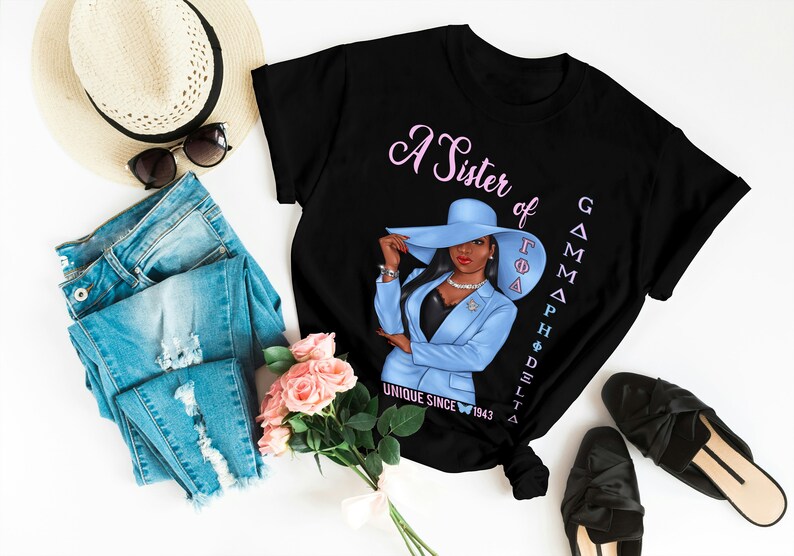 May include: Black t-shirt with a pink and blue illustration of a woman wearing a blue hat and suit. The text "A Sister of Gamma Phi Delta Unique Since 1943" is printed on the shirt.