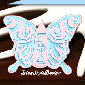 May include: A pink and blue embroidered butterfly patch with the Greek letters "ΓΦΔ" in the center. The patch is on a white surface. "DivaStyleDesign" is written below the patch.