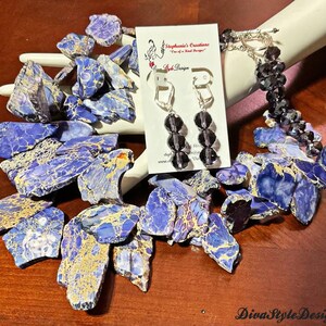 Puede incluir: Un collar de declaraci&oacute;n azul y dorado hecho de piedras grandes de forma irregular. El collar se combina con un brazalete de cristal negro y pendientes a juego. Los pendientes son de estilo colgante con tres cuentas de cristal negro.