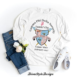 Peut inclure: T-shirt blanc à manches longues avec un écusson Gamma Phi Delta Sorority. L'écusson comprend le texte "Founder's Day" et "Unique Since February 1943". Le t-shirt est associé à un jean bleu et des baskets blanches.
