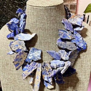 Puede incluir: Un collar llamativo hecho de piedra de jaspe azul y dorada. El collar est&aacute; hecho de muchas piezas de piedra de forma irregular que est&aacute;n enhebradas juntas. El collar se muestra en un maniqu&iacute;.
