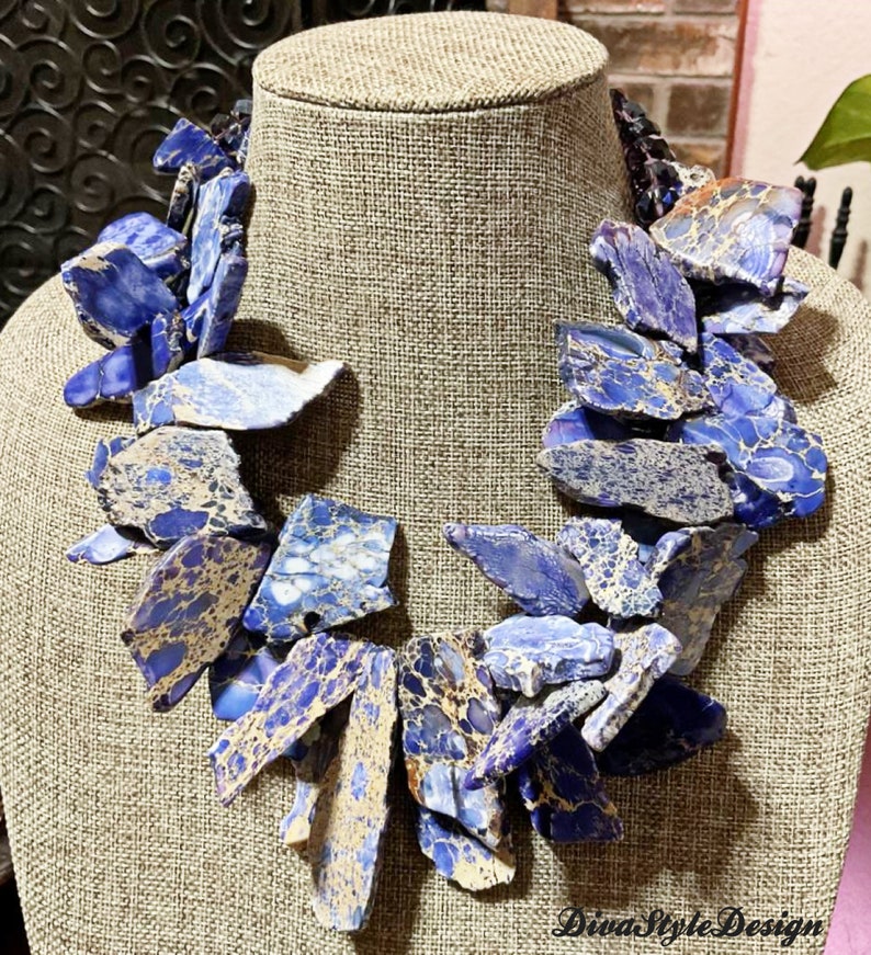 Puede incluir: Un collar llamativo hecho de piedra de jaspe azul y dorada. El collar est&aacute; hecho de muchas piezas de piedra de forma irregular que est&aacute;n enhebradas juntas. El collar se muestra en un maniqu&iacute;.