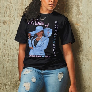 May include: A black t-shirt with a graphic of a woman wearing a blue suit and a hat. The text "A Sister of Gamma Phi Delta" and "Unique Since 1943" are printed on the shirt.