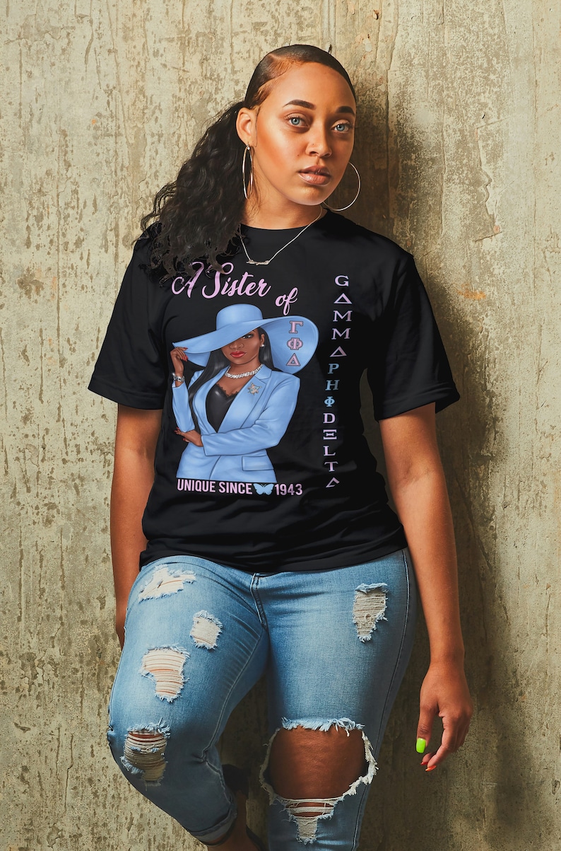 May include: A black t-shirt with a graphic of a woman wearing a blue suit and a hat. The text "A Sister of Gamma Phi Delta" and "Unique Since 1943" are printed on the shirt.