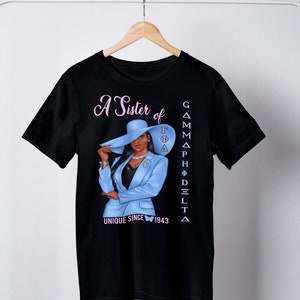 May include: Black t-shirt with a graphic of a woman wearing a blue suit and a hat. The text "A Sister of Gamma Phi Delta Unique Since 1943" is printed on the shirt.