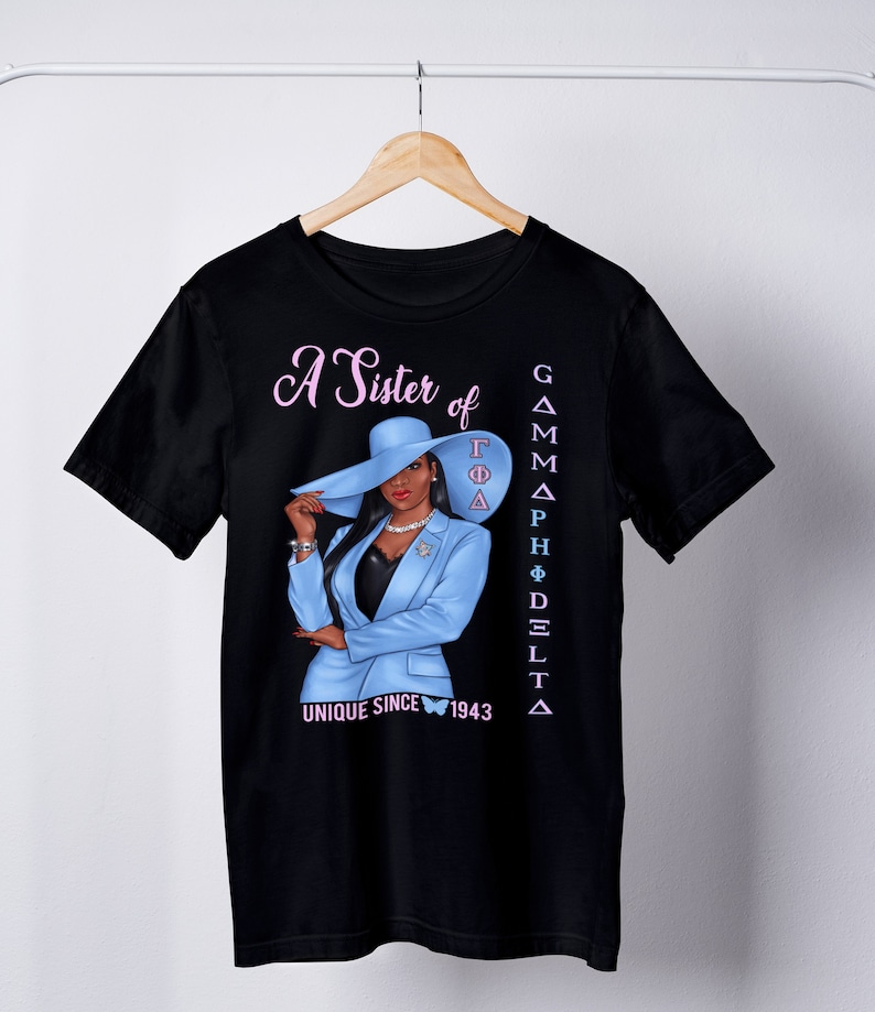 May include: Black t-shirt with a graphic of a woman wearing a blue suit and a hat. The text "A Sister of Gamma Phi Delta Unique Since 1943" is printed on the shirt.