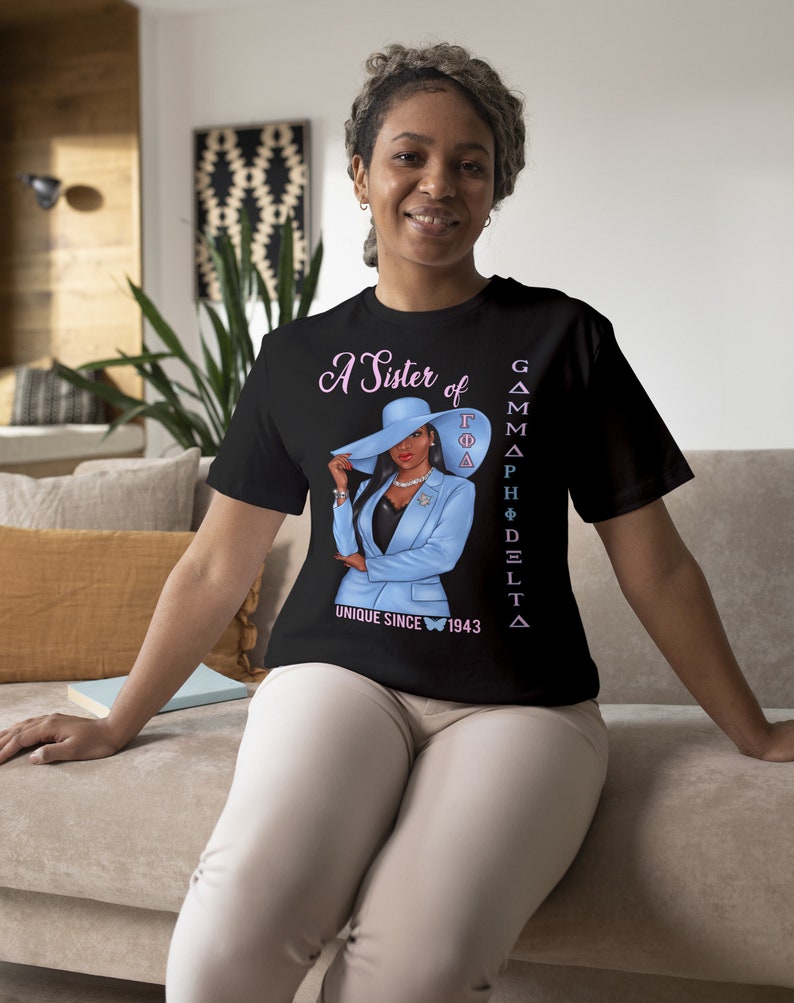 May include: A black t-shirt with a graphic of a woman wearing a blue suit and a hat. The text "A Sister of Gamma Phi Delta Unique Since 1943" is printed on the shirt.