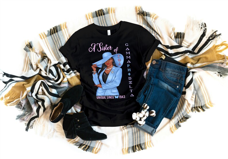 May include: Black t-shirt with a graphic of a woman wearing a blue suit and a hat. The text "A Sister of Gamma Phi Delta Unique Since 1943" is printed on the shirt.