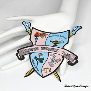 May include: A pink and blue embroidered patch with a crest featuring a torch, an open book, a rose, a dove, and a scale. The text "FOUNDED 1943 LEWIS BUSINESS COLLEGE" is on a banner around the crest.