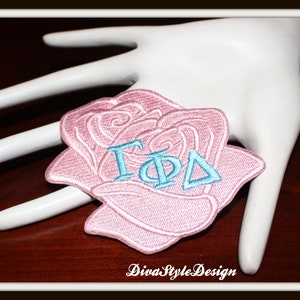 May include: A pink embroidered rose with the Greek letters "ΓΦΔ" in light blue.